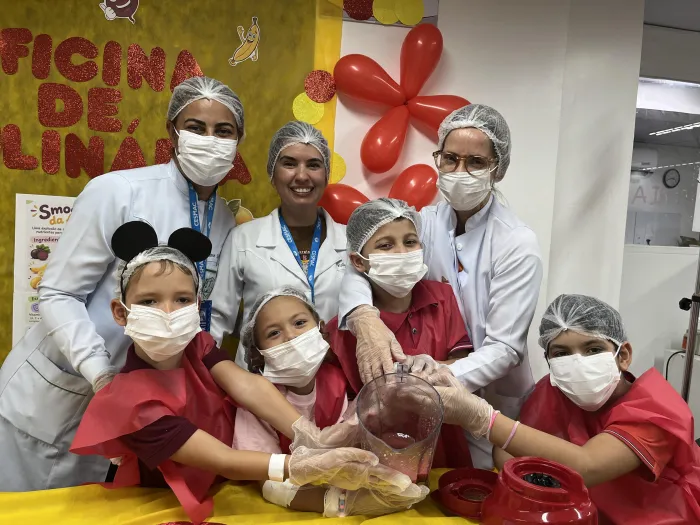 A nutricionista Rosemary Caldas, ao lado das estudantes Kelly Vieira e Viviane Silva, apresenta o Smoothie da Alegria às crianças - Natália Lessa